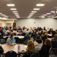 A large group of students sitting at round tables and facing a speaker